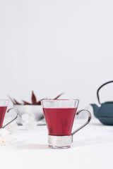 Una taza transparente de té de bayas con tetera de hierro azul sobre una mesa blanca y un fondo gris claro	