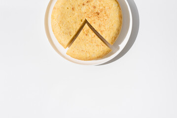 Tortilla de patatas española hecha con aceite de oliva, huevos y patatas en un plato blanco sobre una mesa blanca. Aperitivo español. Vista superior