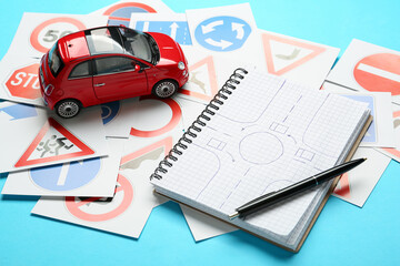 Many different road sign cards, notebook with sketch of roundabout and toy car on light blue background. Driving school - Powered by Adobe