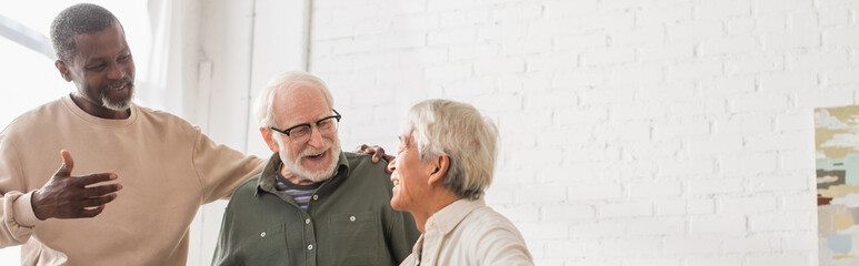 Positive multiethnic friends talking to senior asian man at home, banner.