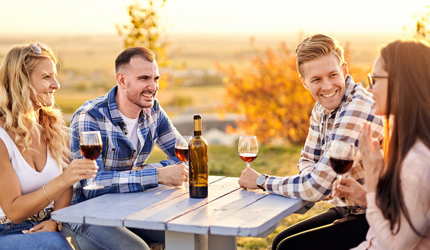 Young friends having fun outdoors - Happy people enjoying harvest time together at farmhouse winery countryside - Youth and friendship concept - Tasting red wine at vineyard before sunset