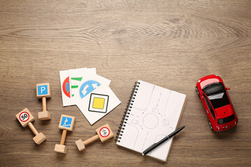 Many different road signs, notebook and toy car on wooden background, flat lay with space for text....