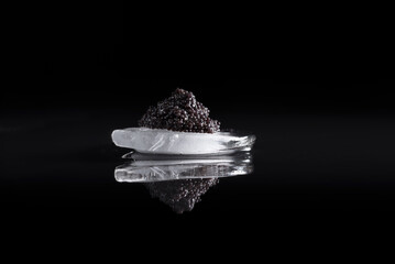 Caviar negro de esturión sobre una piedra de hielo reflejada en fondo negro. Comida delicatessen...