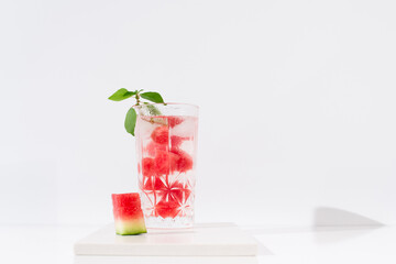 Un vaso de jugo de sandía desintoxicante con hojas verdes trozos de sandia y hielo sobre fondo claro