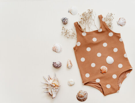 Little girl's cute swimsuit with sunglasses and seashells on beige background. Retro fashion baby, summer holidays concept