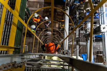 A helmeted employee walks down a vertical iron ladder to his colleagues. © CjVitoS