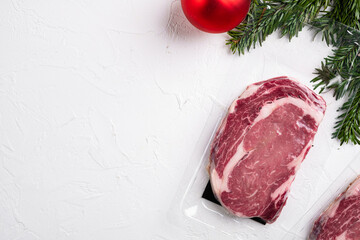 Rib-eye beef steak in plastic packing tray with Christmas tree decorations, on white stone table...
