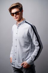 Obraz premium Portrait of handsome guy standing in sunglasses holds arms in pockets, isolated on a gray background