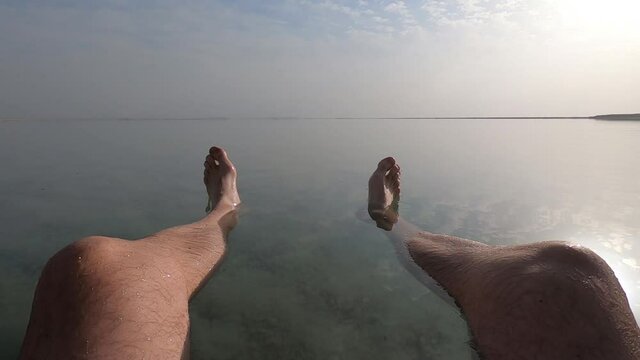 Low angle view of legs of man floating in the Dead Sea, due to high salt levels. Natural spa treatment and healing powers. 
