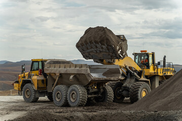A loader loads ore into an articulated dump truck. - obrazy, fototapety, plakaty