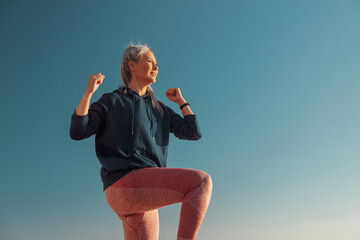 Active female in pink leggins and blue hoodie exercising , lifting one knee up and looking ahead on...