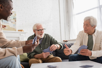 Elderly multiethnic men playing cards in living room.