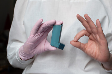 A woman's hand in a glove, the doctor's hand holds an asthma inhaler. Using a blue asthma inhaler to relieve an asthma attack
