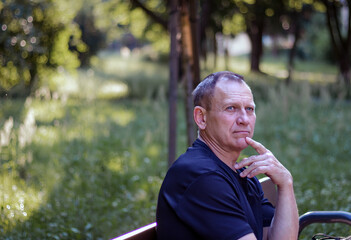 portrait of a serious pensive middle-aged man sitting on a park bench