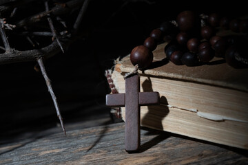 Close up rosary, ancient Bible and thorn wreath as symbol of death and resurrection of Jesus Christ. Conceptual image with deep shadows.