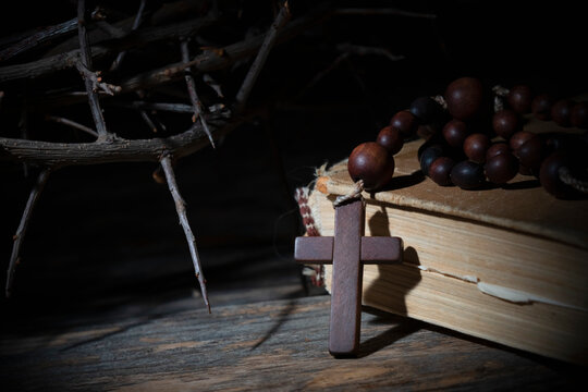 Rosary, ancient Bible and thorn wreath as symbol of death and resurrection of Jesus Christ. Conceptual image with deep shadows.