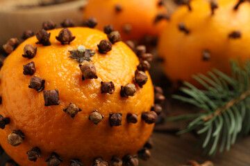 Pomander balls made of tangerines with cloves and fir branch on wooden table, closeup