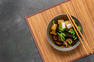 Miso soup. Japanese vegetarian soup with tofu, shiitake mushrooms and seaweed in a bowl on a bamboo mat. Dark grunge background. Top view.