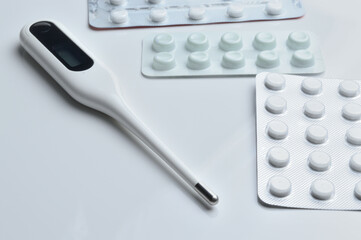 tablets in a package and a white electronic thermometer on a white surface close-up.