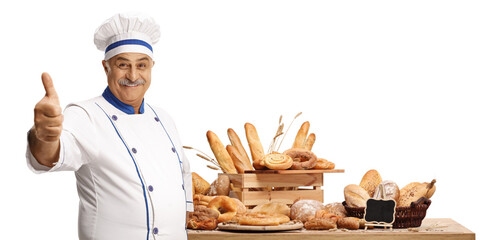 Mature male baker posing in front of a table with breads and gesturing thumbs up