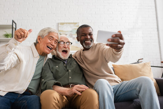 Smiling multiethnic friends using smartphone on couch at home.
