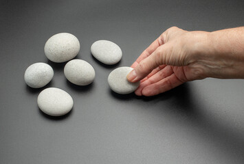 White stones on a dark background. A woman's hand holds one stone. Concept of spa procedures, massage, fortune telling on ancient runes