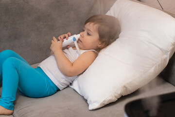 A small child with a thermometer lies next to a humidifier and tries to be treated.