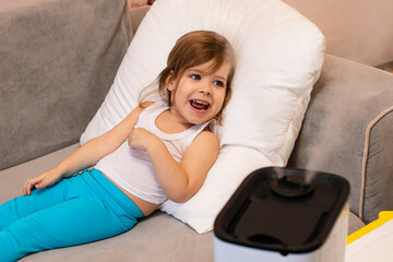 A small child with a thermometer lies next to a humidifier and tries to be treated.