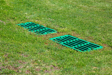 catch basin grate drainage on the lawn with green grass septic tank cover, two rectangular green...