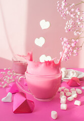 Pink splash in a transparent cup from falling heart-shaped marshmallows on a pink background surrounded by hearts and flowers, valentine's day, march 8, holiday, milk