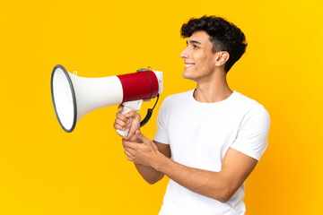 Young Argentinian man isolated on yellow background shouting through a megaphone to announce...