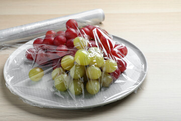 Plate of fresh grapes with plastic food wrap on wooden table, closeup