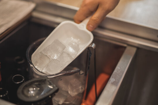 Barista with scoop taking ice cubes from container