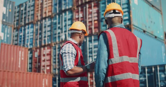ndustrial Engineer with Tablet and Black African American Male Supervisor in Hard Hats and Safety Vests Stand in Container Terminal. Colleagues Talk About Logistics Operations