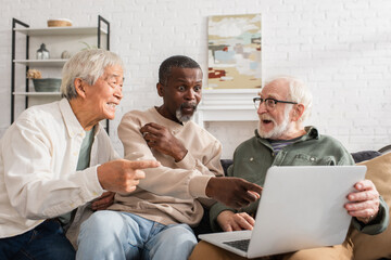 Obraz premium Excited african american man pointing at laptop near multiethnic friends at home.