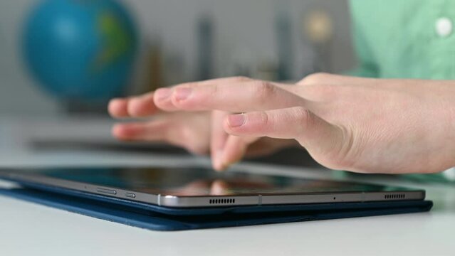 Close up 4K 60fps video of child tapping tablet doing homework at online course