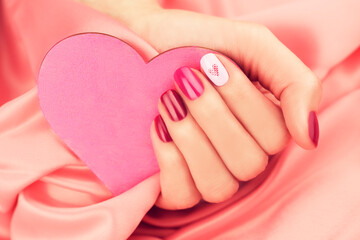 A woman's hand with pink and lilac manicure holding a heart. Valentine's Day.
