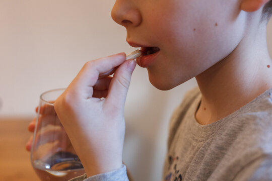 A child taking a pill and holding a glass of water