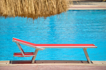 Fototapeta premium Empty deck chair on swimming pool side in summer resort. Vacations and getaway concept