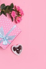 Pink gift box with blue bow on pink background with pink roses and chocolate sweets . Valentine's Day. Mother's Day.