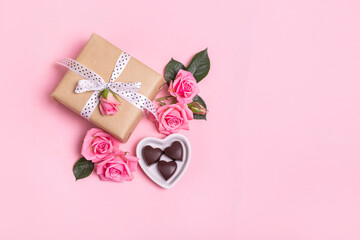 Craft gift box with white bow on pink background with pink roses and chocolate sweets . Valentine's Day. Mother's Day.