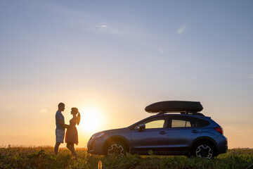 Obraz na płótnie Canvas Happy couple standing near their car at sunset. Young man and woman enjoying time together travelling by vehicle