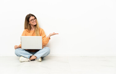 Young woman with a laptop sitting on the floor presenting an idea while looking smiling towards