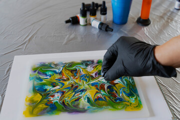 Drawing process with alcohol ink on liquid. A female hand in a glove with a wooden stick makes a...