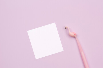 Blank white paper with flamingo shaped pen on  lilac - pink background. space for text