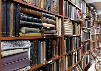 Blurred image of a library with bookcases. Many different books on the shelves. Large selection of books in a bookcase. Blurred background.