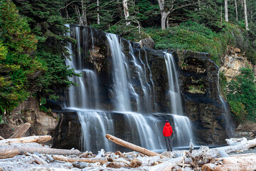 Hiker figure wearing a red jacket in front of Tsusiat Falls along the West Coast Trail, Pacific Rim...