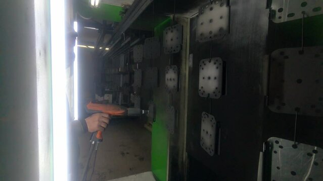Worker paints metal parts in a factory