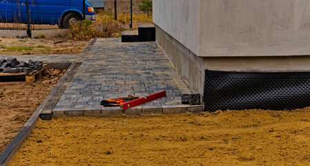 Budowa chodnika ( brukowanie ) . Podbudowa piasek + cement , częściowo ułożona kostka  , młotek brukarski poziomica i rękawice .