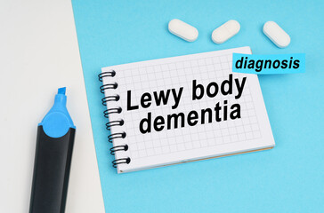 On a white and blue surface are pills, a marker and a notebook with the inscription - Lewy body dementia